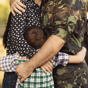 A man in military uniform embraces a woman and a child, displaying love and affection in a heartwarming moment- Moss Bollinger LLP