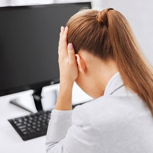 A woman in distress sits at a desk, her head buried in her hands, overwhelmed by the situation- Moss Bollinger LLP