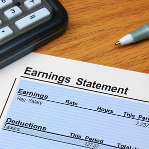 Earnings statement on desk with calculator: financial document displaying income and expenses- Moss Bollinger LLP