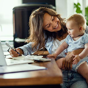 A woman sitting at a desk with a baby, engrossed in her work while the baby peacefully observes- Moss Bollinger LLP