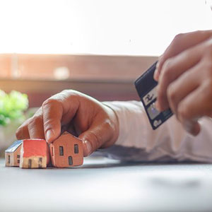 A person holds a credit card and a miniature house, symbolizing the connection between location and renters insurance rates- Moss Bollinger LLP