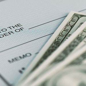 A close-up of a check with “PAY TO THE ORDER OF” visible, and a $100 bill on top- Moss Bollinger LLP