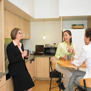 Three professional women in business attire engaged in a conversation in a kitchen setting- Moss Bollinger LLP