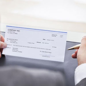 A man sitting at a desk, holding a check in his hand- Moss Bollinger LLP