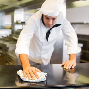A chef cleaning a restaurant counter with a cloth, ensuring cleanliness and hygiene- Moss Bollinger LLP