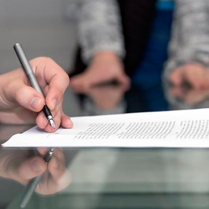 A person signing a document on a table. Image may depict signing an "Independent Contractor" agreement- Moss Bollinger LLP