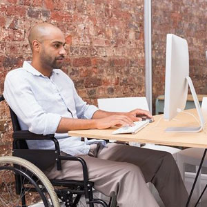 A man in a wheelchair using a computer at a desk- Moss Bollinger LLP