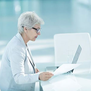 A woman wearing glasses sits at a table, focused on her laptop- Moss Bollinger LLP