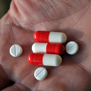 A hand holds red and white capsules and small white tablets- Moss Bollinger LLP