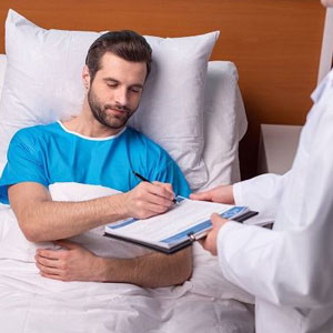 Person in blue shirt sits up in bed, white-coated individual notes on clipboard in a medical setting- Moss Bollinger LLP