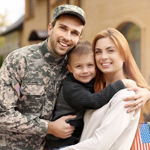 A soldier and his family smiling in front of their house, capturing a moment of love and togetherness- Moss Bollinger LLP