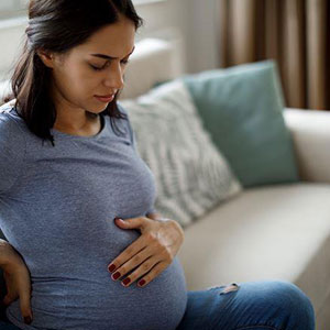 A pregnant woman sitting, holding her belly, in a indoor setting- Moss Bollinger LLP