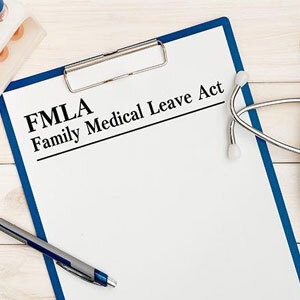 A clipboard with “FMLA Family Medical Leave Act” paper, pen, and stethoscope on wooden surface- Moss Bollinger LLP