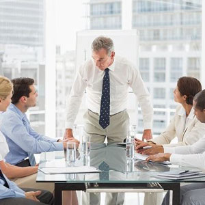 Supervisor leads a formal meeting at a glass table in a bright office with professionals in formal attire- Moss Bollinger LLP
