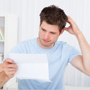 A person in a blue shirt, holding a paper. Scratching head, looking puzzled. Bright background- Moss Bollinger LLP