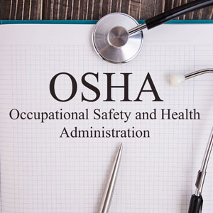 Bold 'OSHA' acronym on grid paper, 'Occupational Safety and Health Administration' in smaller font. Stethoscope, pen on wooden surface- Moss Bollinger LLP