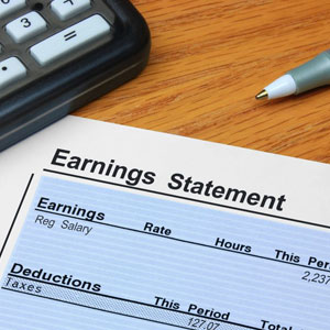 Earnings statement with salary, deductions, and taxes. Calculator and pen nearby- Moss Bollinger LLP