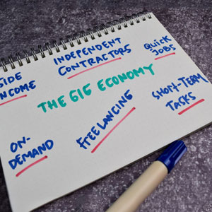 Gig Economy Notebook: Open on textured surface, highlighting side income, independent contractors, quick jobs, freelancing, short-term tasks, on demand. Captures flexible, short-term work essence- Moss Bollinger LLP