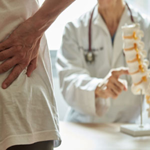 A person with back pain consulting a doctor with a spine model- Moss Bollinger LLP