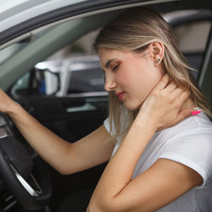 A woman in a car, holding her neck in discomfort while driving - Moss Bollinger LLP