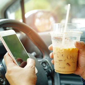A man holding coffee glass and using smartphone while driving - Moss Bollinger LLP