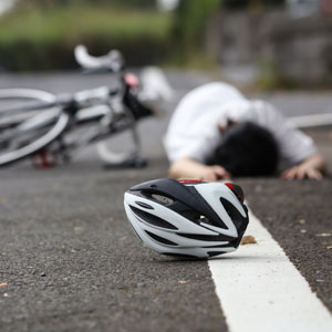 A man lying on the ground next to a bicycle helmet - Moss Bollinger LLP