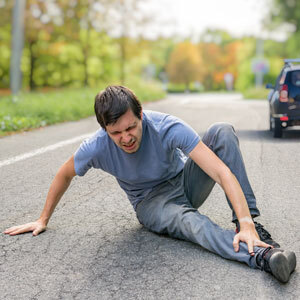 A man kneeling on the road with his car in the background - Moss Bollinger LLP - Pedestrian Accident Lawyer