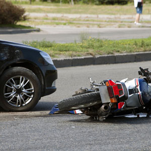A motorcycle and a car on the ground after a collision, with the motorcycle lying next to the car.  - Moss Bollinger LLP